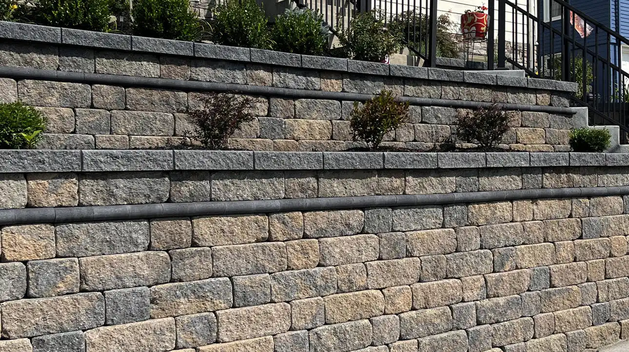 Multi-tier Versa-Lok Weathered Wall Block retaining wall with tan and gray tumbled stone blocks and dark cap course in a residential landscape